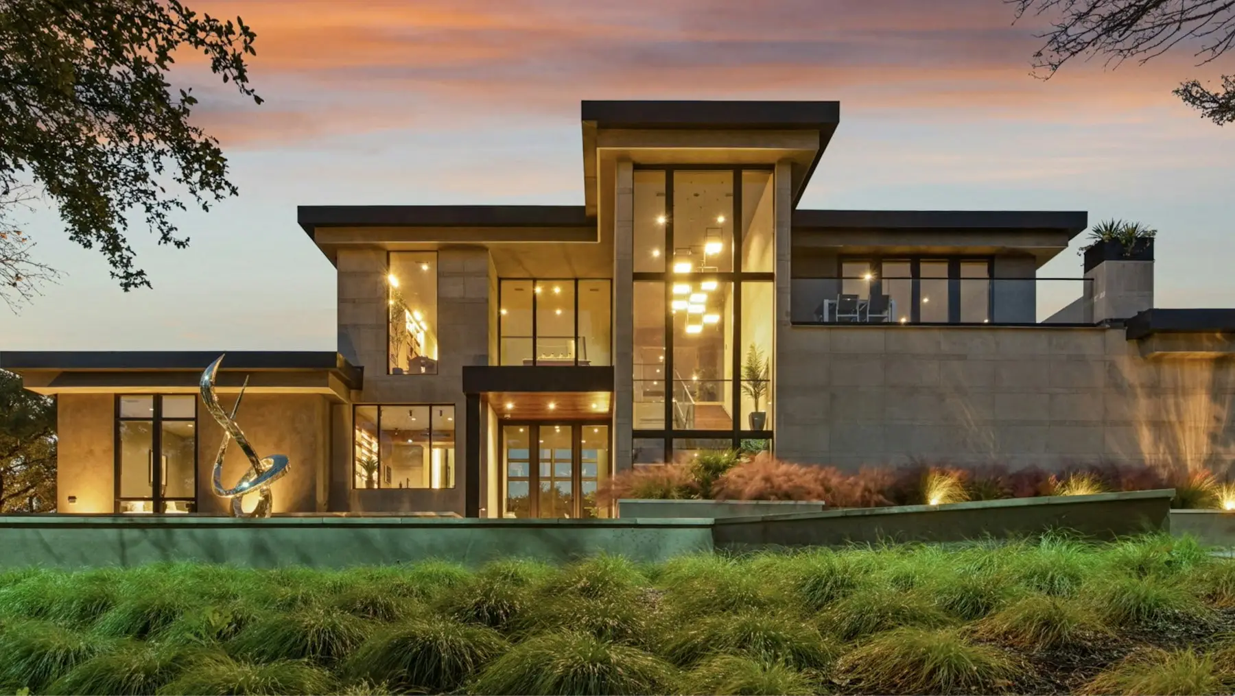 A modern hill-country house at dusk, its tall windows lit warm from inside