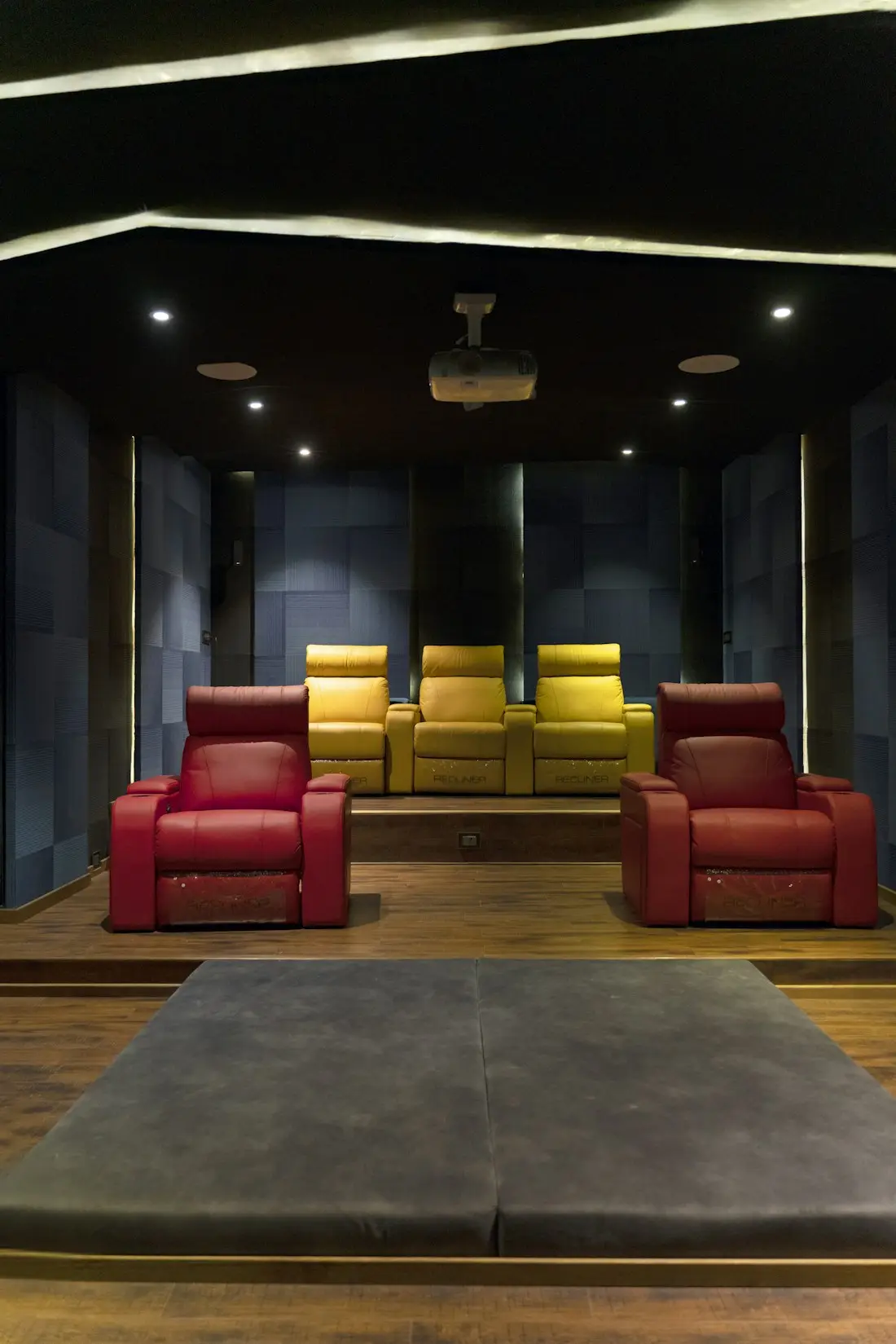 A dark media room with a row of red recliners facing a large screen