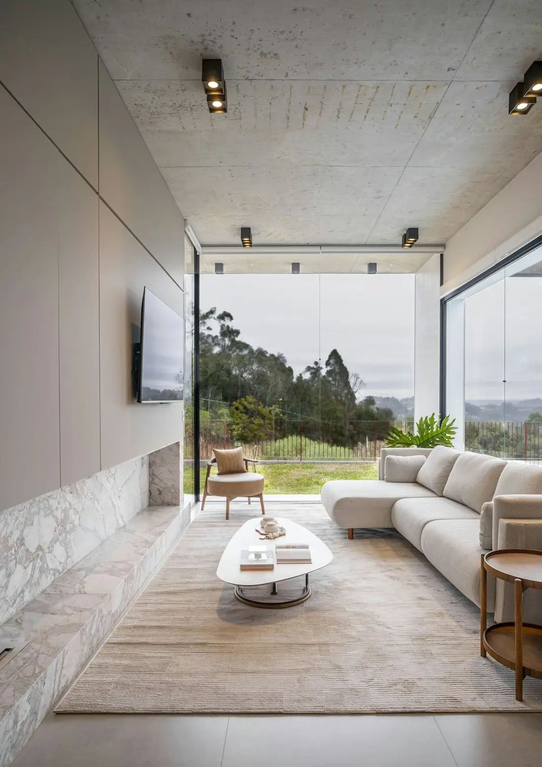 An open living room with a long sofa facing a wall of glass and green hills