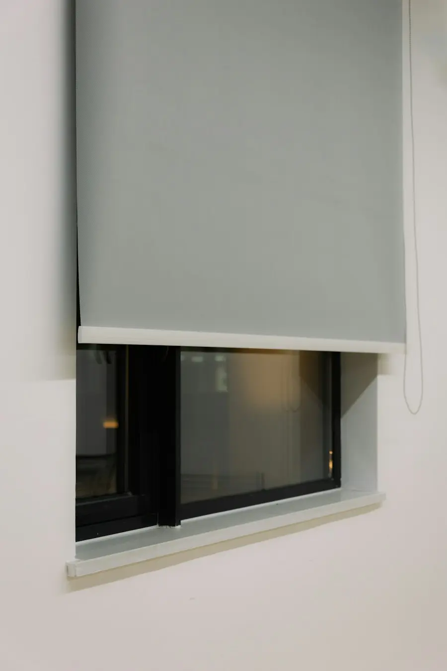 A grey roller shade drawn partway down a modern window