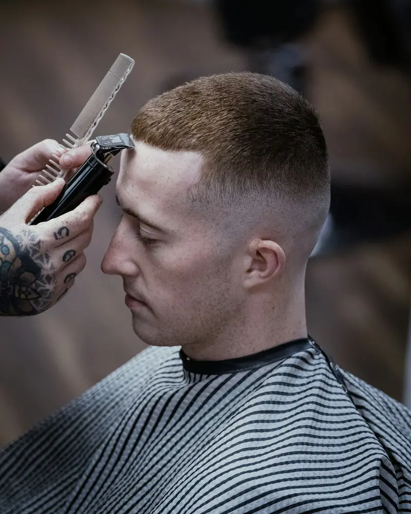 A barber with a tattooed hand blending a skin fade into a short crop