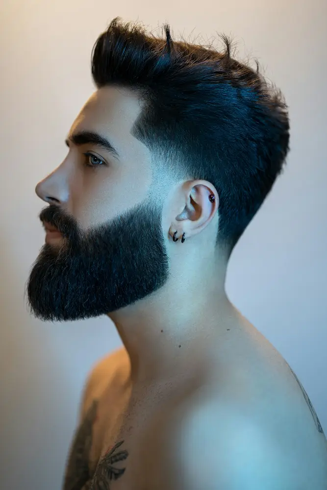 A profile of a man with a full, squared-off beard and a sharp cheek line