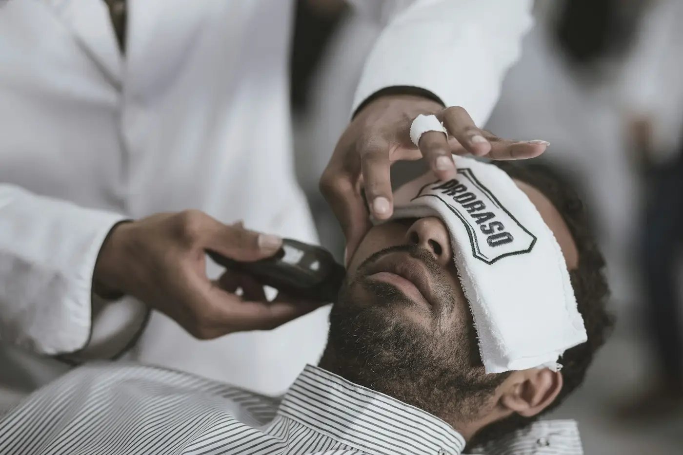 A client reclined with a hot towel over his eyes while the barber lathers his jaw