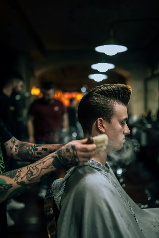 A barber shaping a tall pompadour with tapered sides in a dim shop