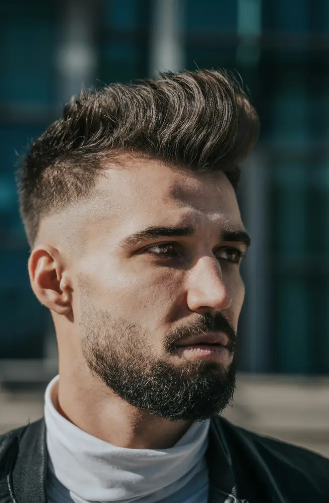 A man with a swept-up quiff and a full beard faded into the sideburns