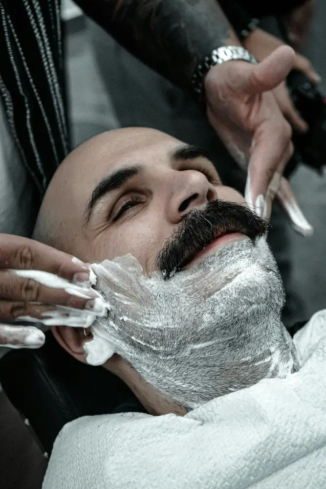 A client reclined under lather while a straight razor clears the cheek