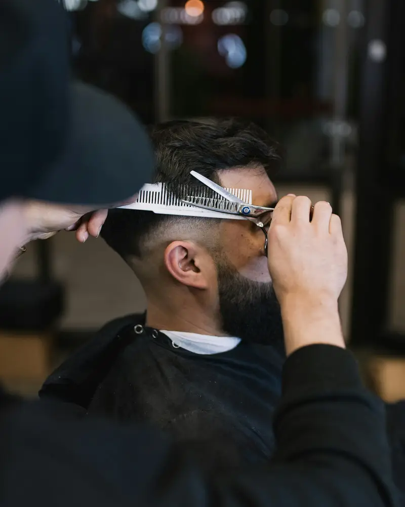 Scissors and a comb lifting dark hair at the crown