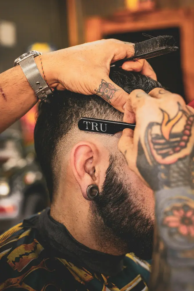 A tattooed forearm holding a straight razor to the side of a client’s head