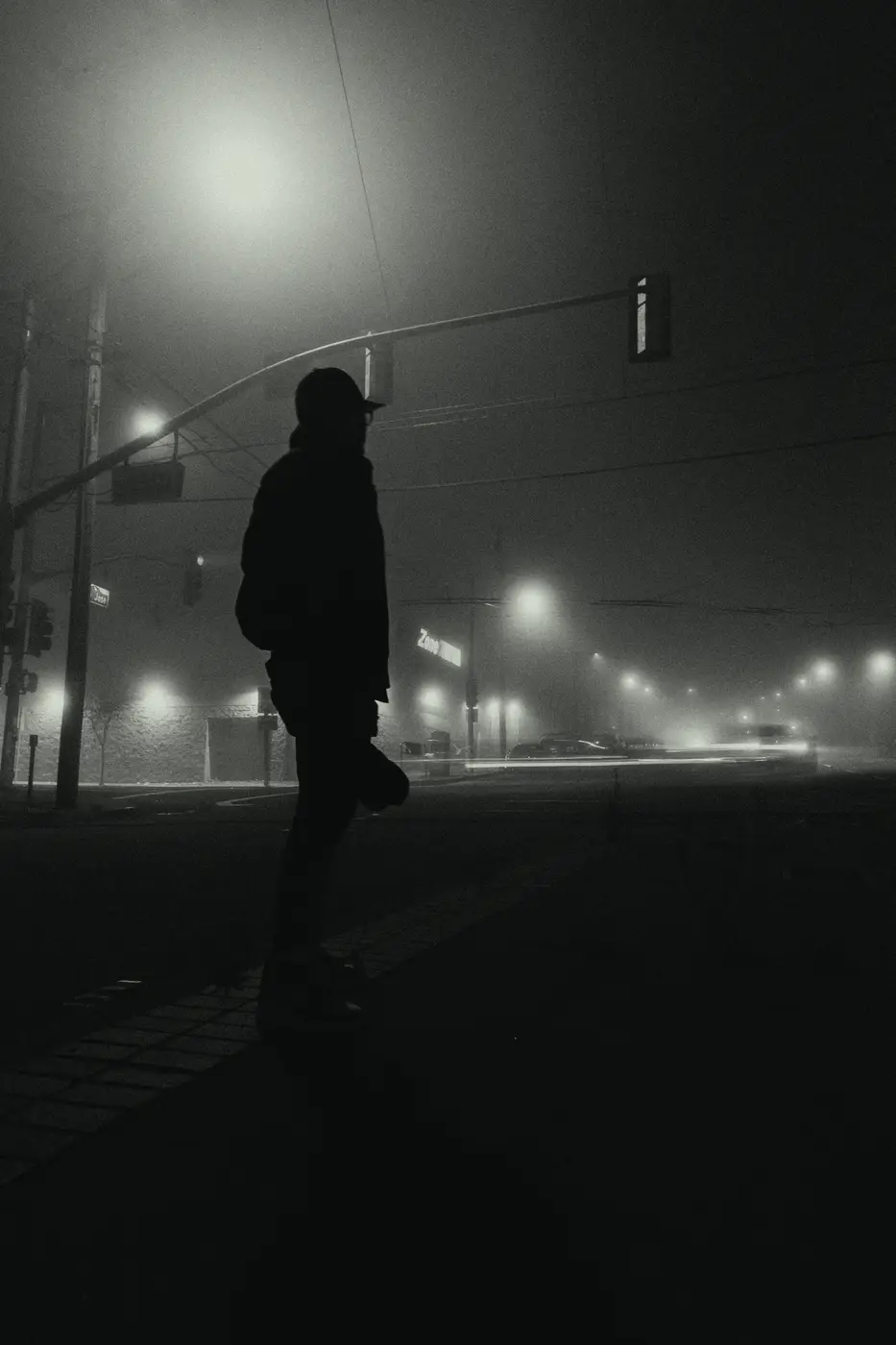 A hooded figure under a streetlight in heavy fog